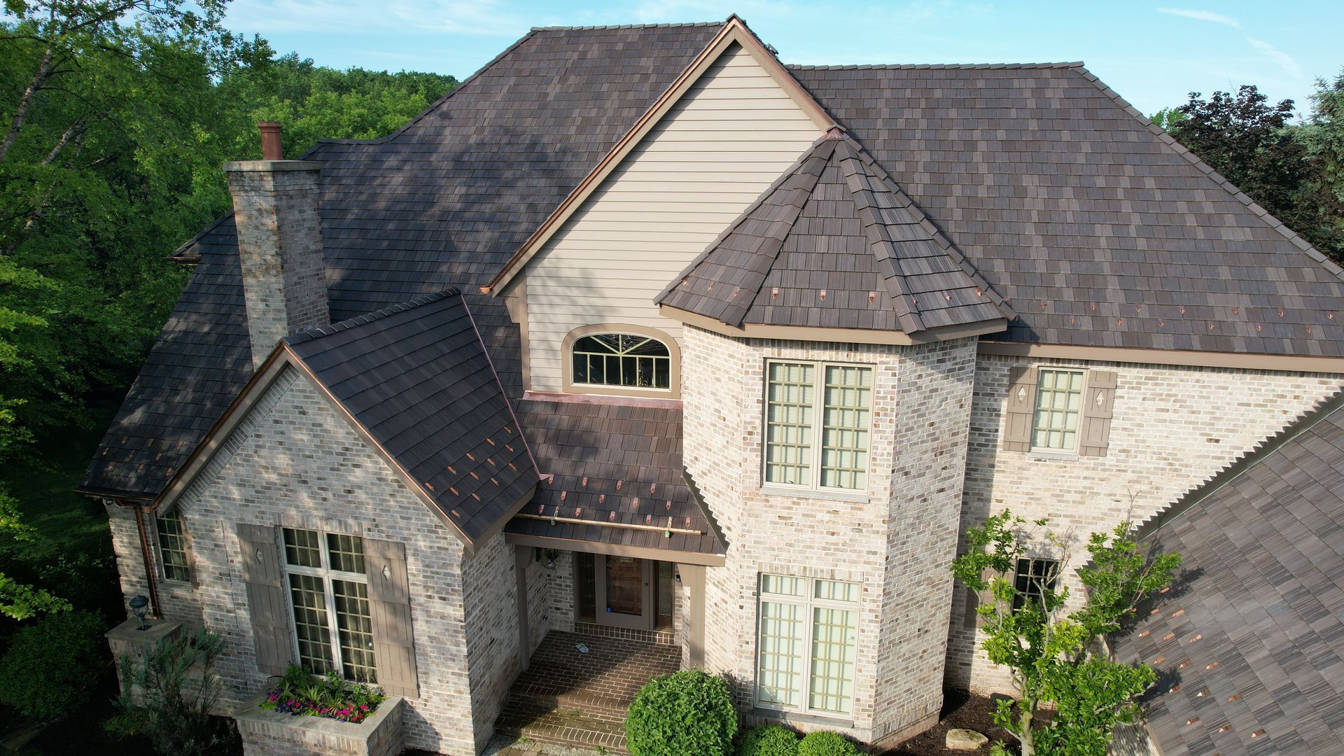 An aerial view of a large brick house with a gray roof surrounded by trees.