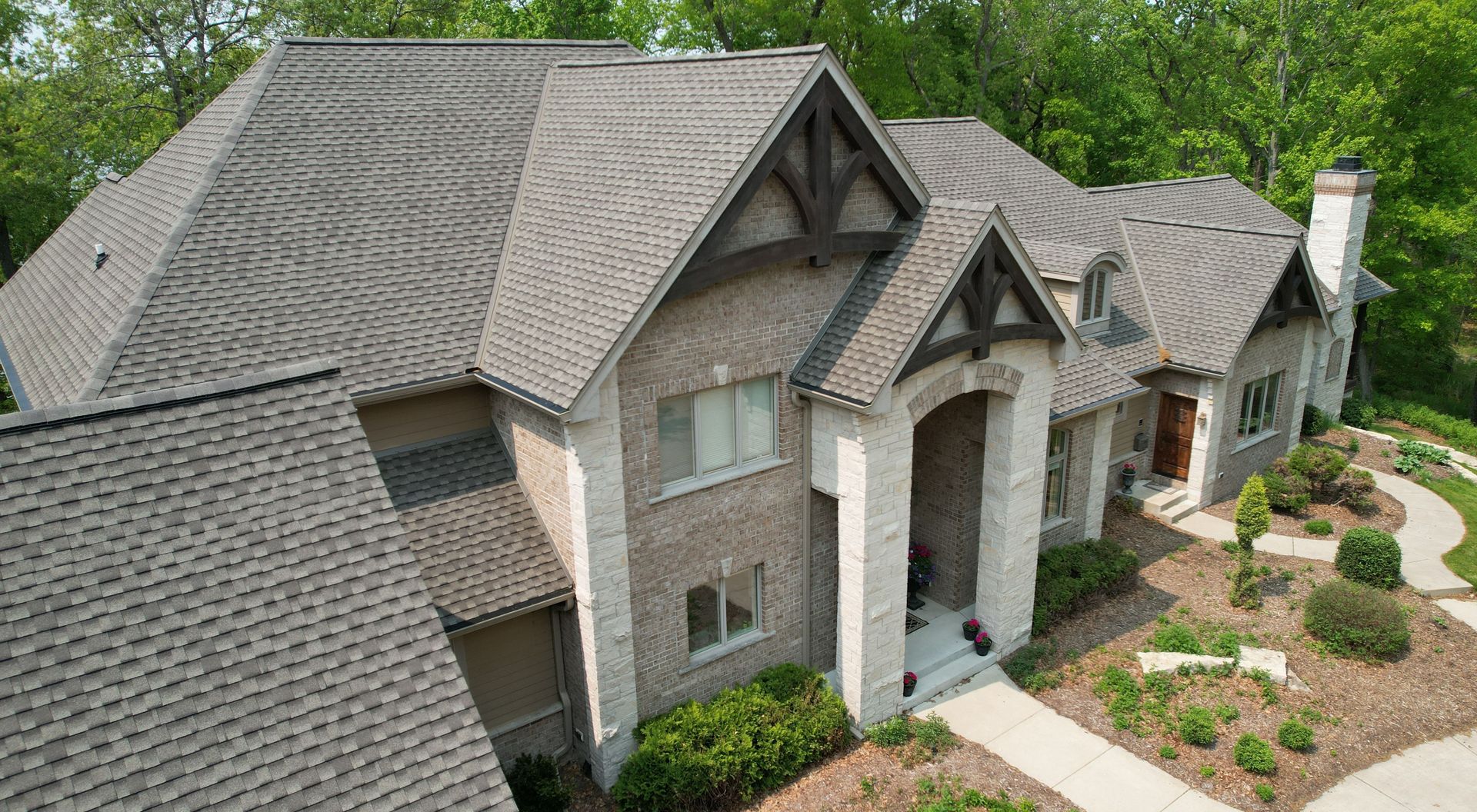 An aerial view of a large brick house with a gray roof surrounded by trees.