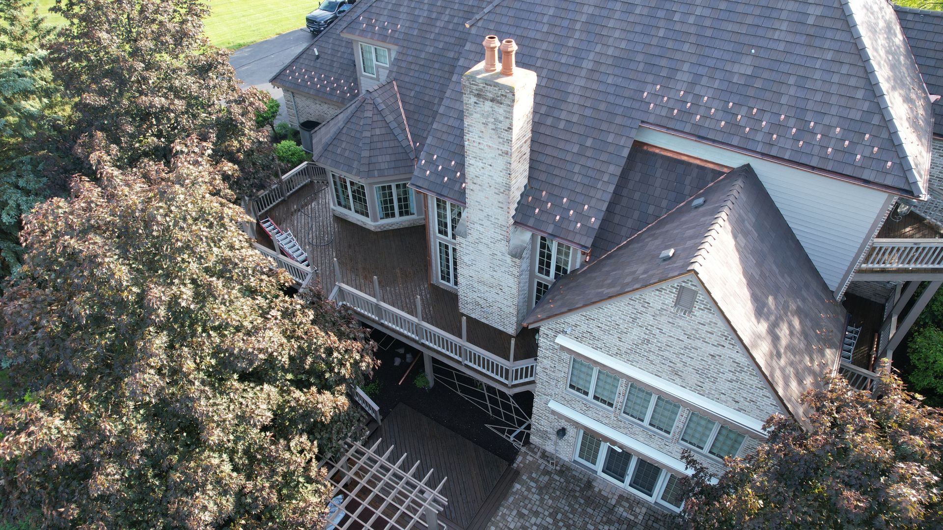An aerial view of a large brick house with a large deck surrounded by trees.