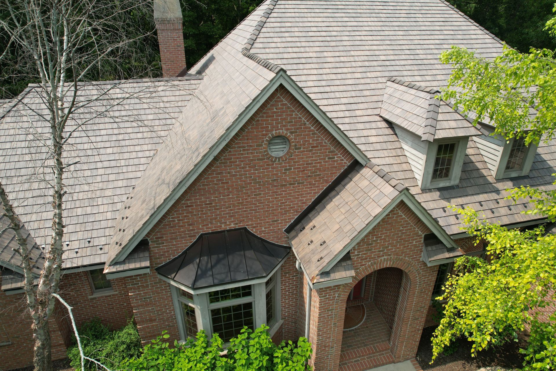 An aerial view of a large brick house with a roof surrounded by trees.