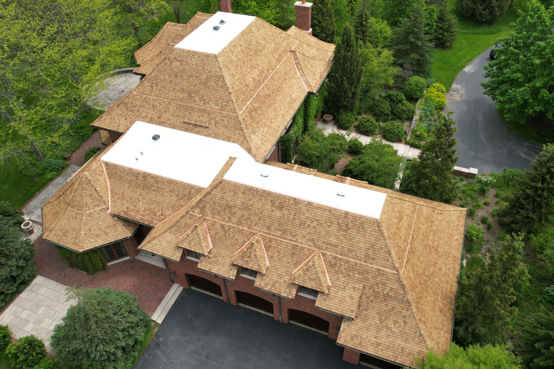 An aerial view of a large house with a white roof surrounded by trees.