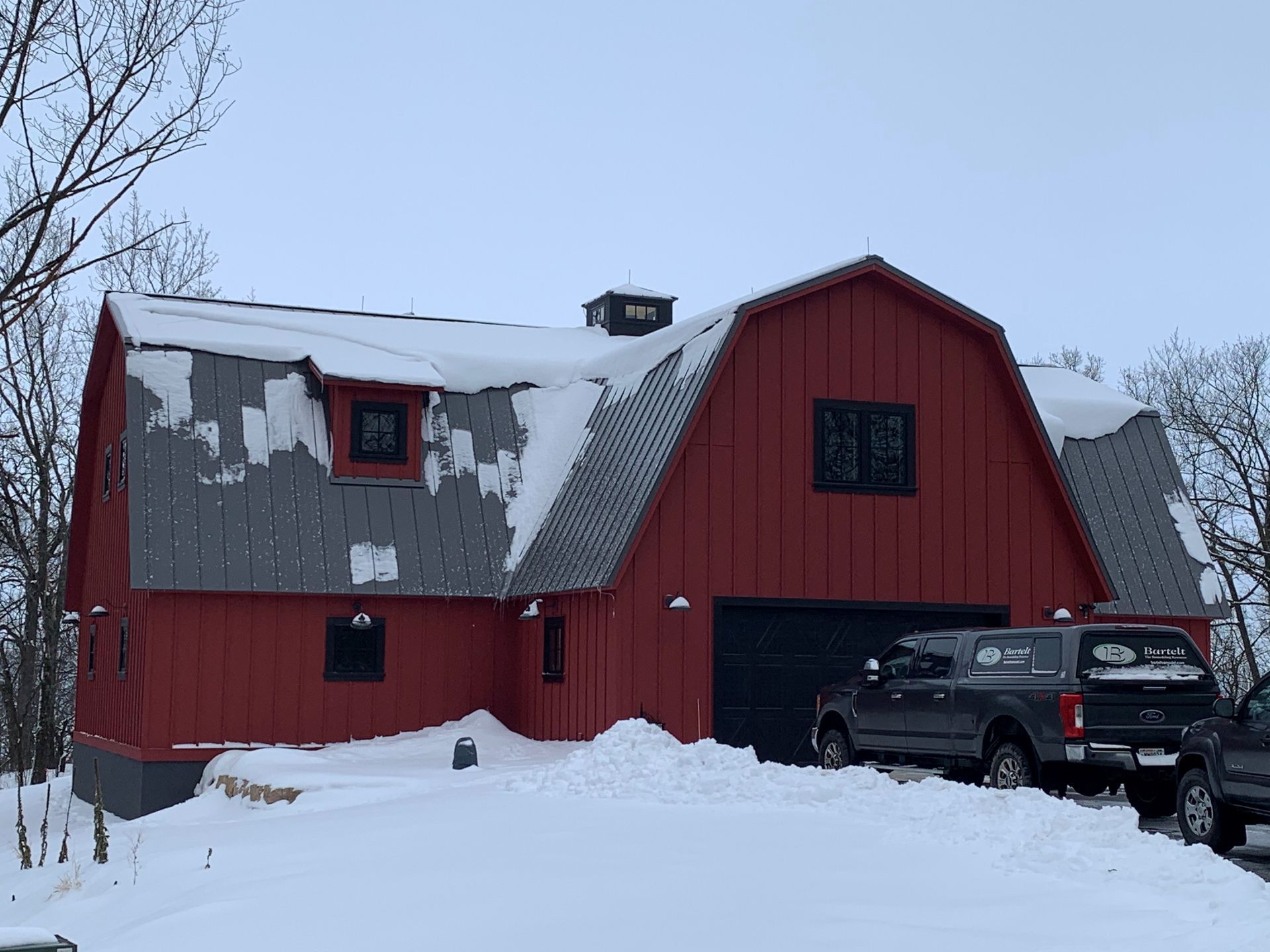 A red barn with a black truck parked in front of it in the snow.