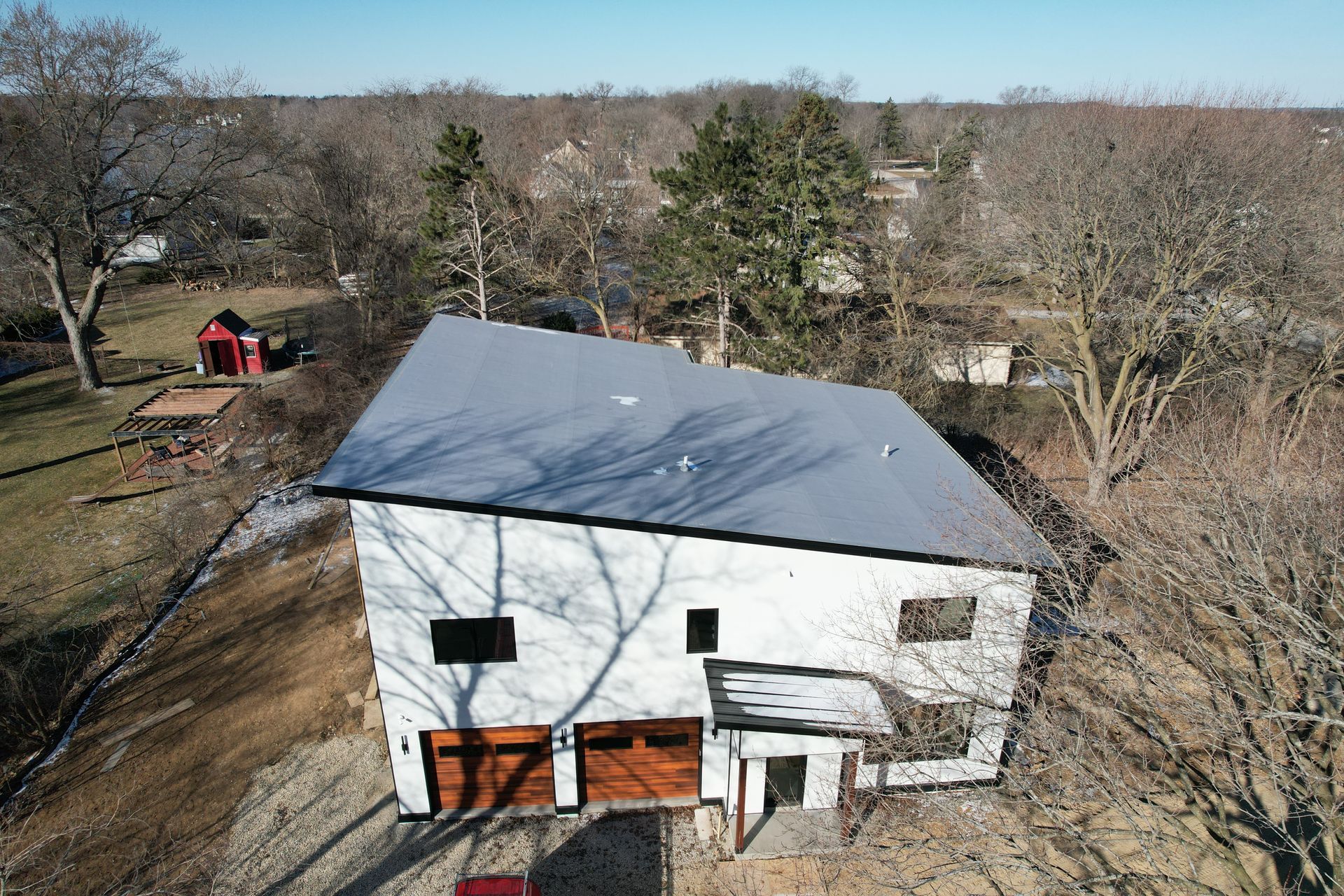 An aerial view of a white house with a metal roof surrounded by trees.