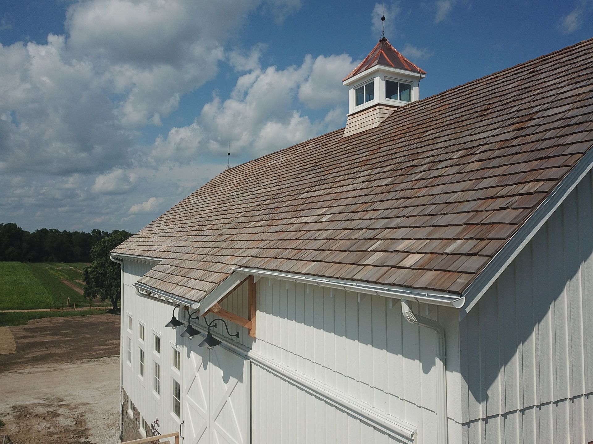 A white barn with a wooden roof and a weather vane on top.