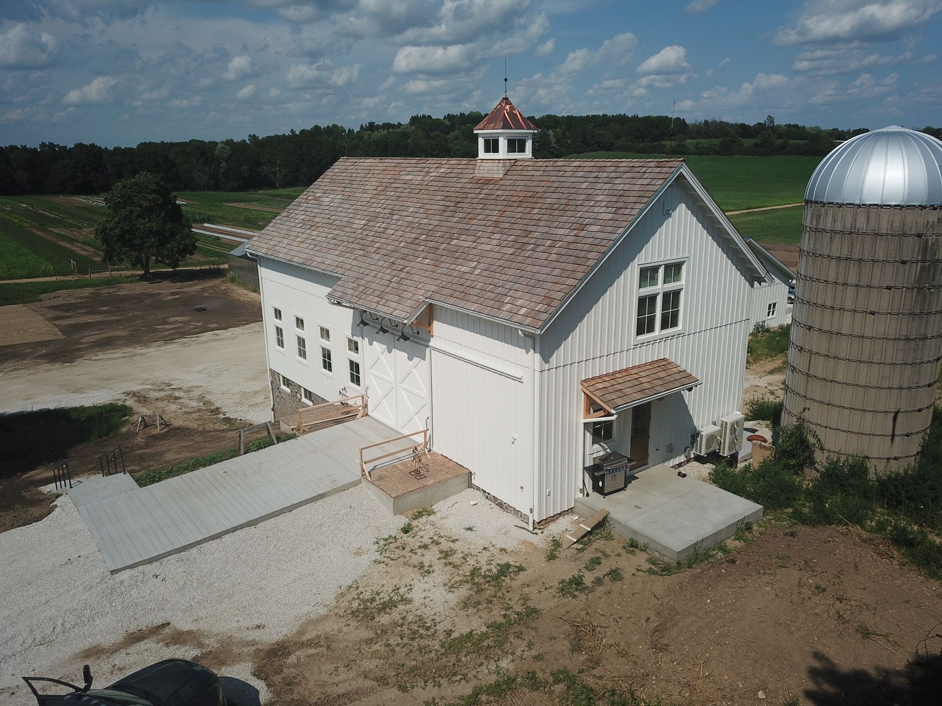 An aerial view of a white barn with a silo in the background.