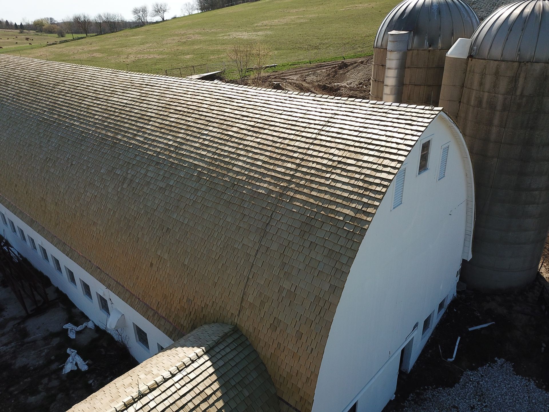 An aerial view of a barn with silos in the background.