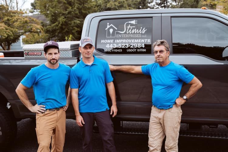 Three men in blue shirts are standing next to a truck.