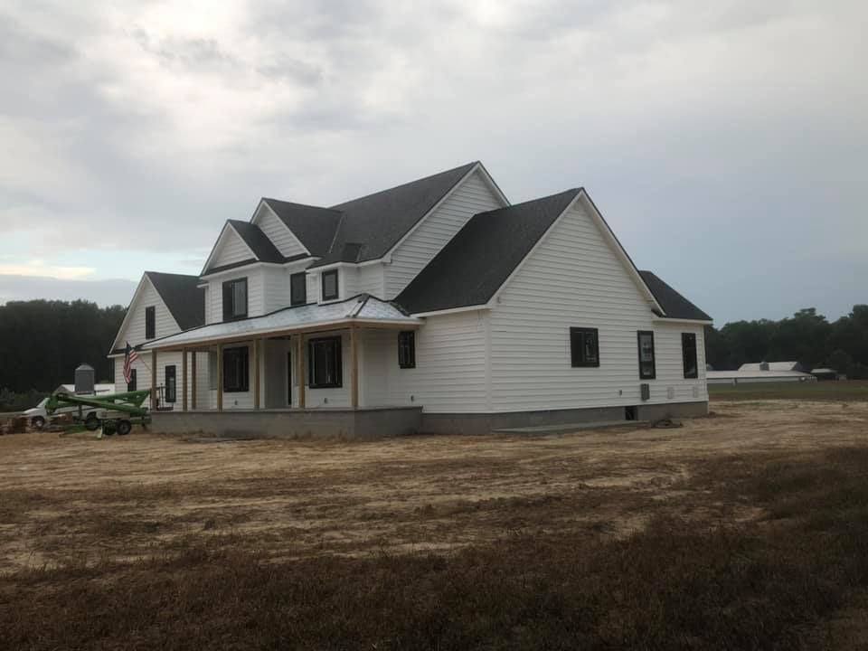 A large white house with a black roof is sitting in the middle of a field.