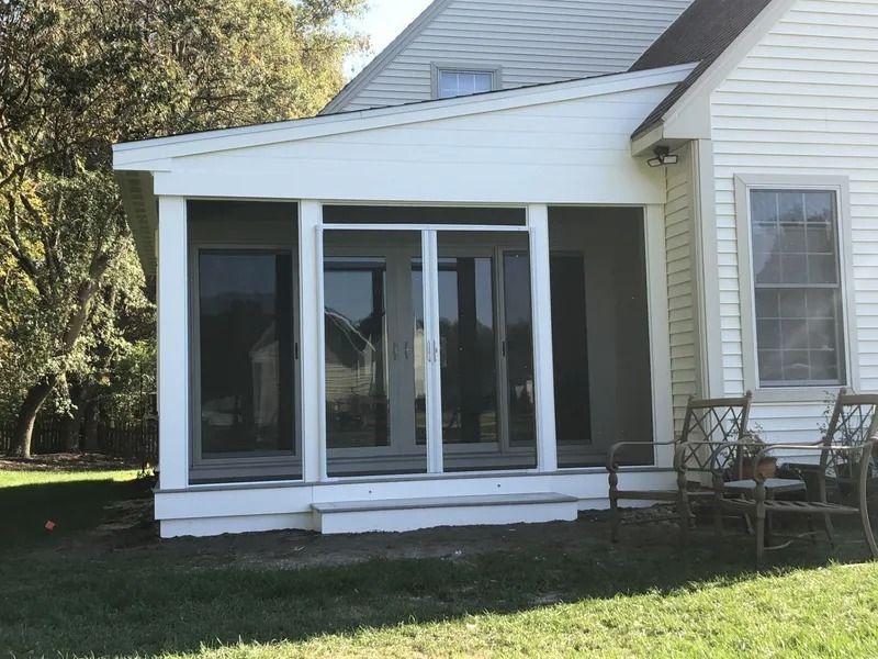 White screened porch attached to a white house with sliding glass doors and seating.