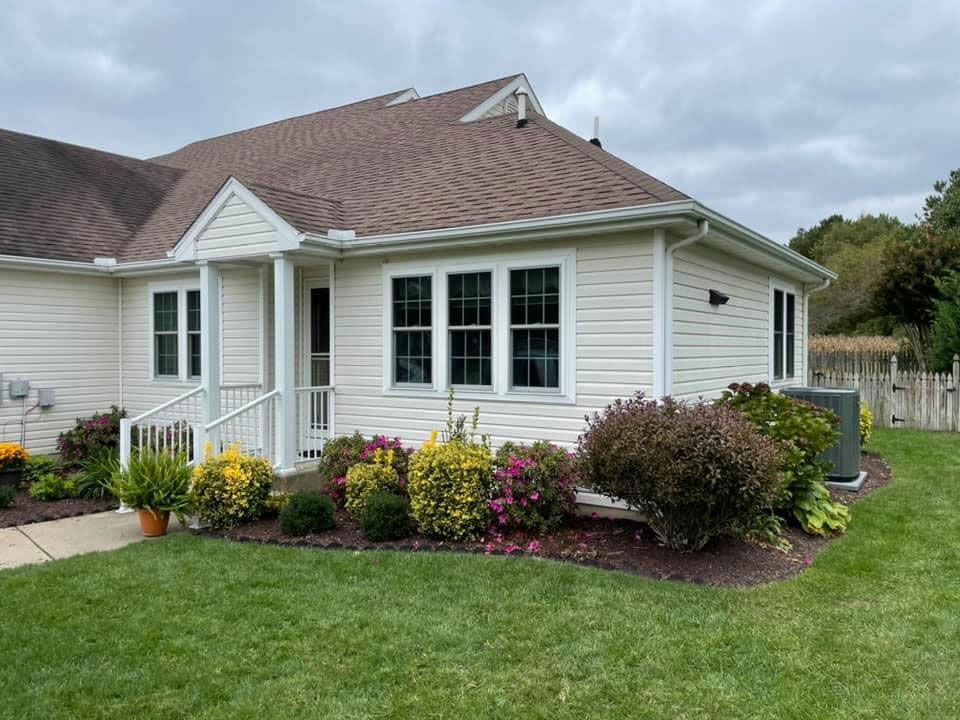 A white house with a brown roof is sitting on top of a lush green lawn.