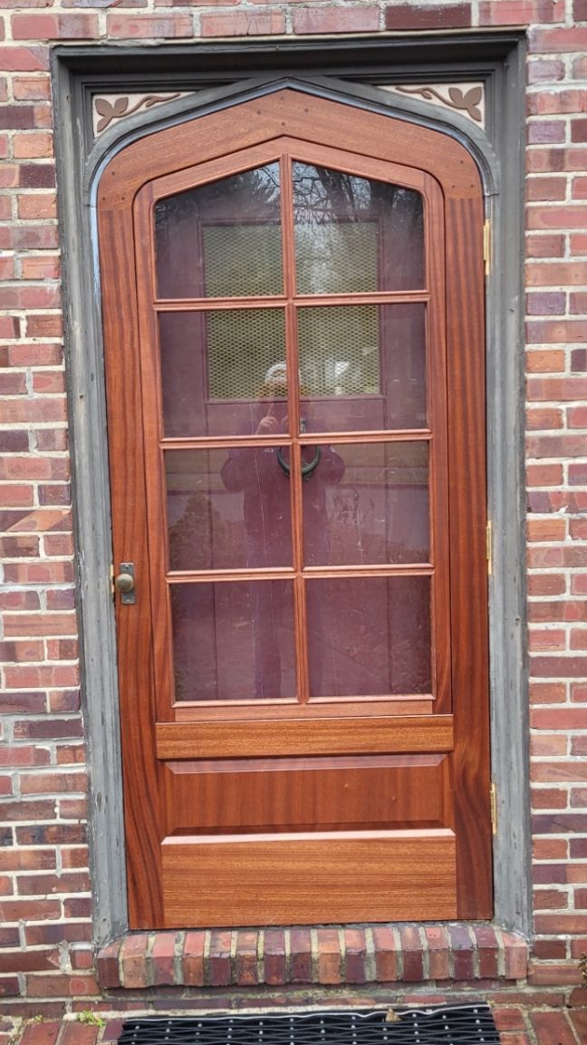 A wooden door with a screen on it is on a brick wall.