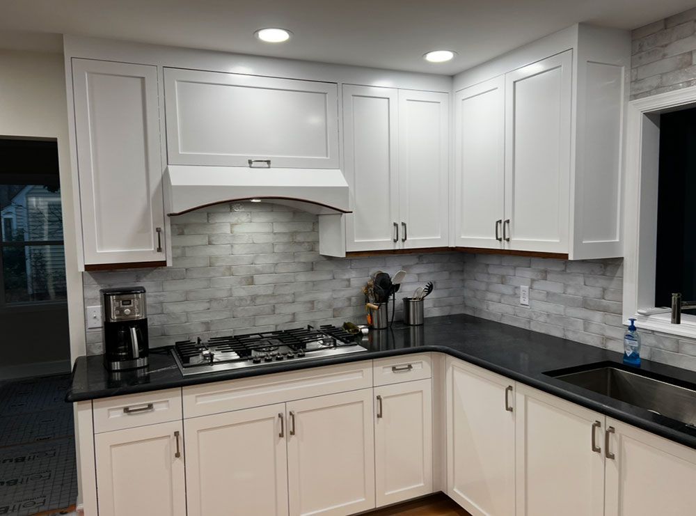 A kitchen with white cabinets and black counter tops.