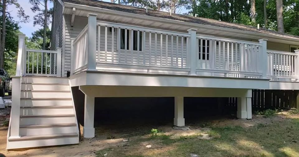 A white house with a large deck and stairs.