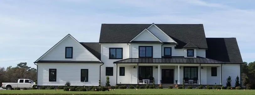 A large white house with a black roof and a white truck parked in front of it.