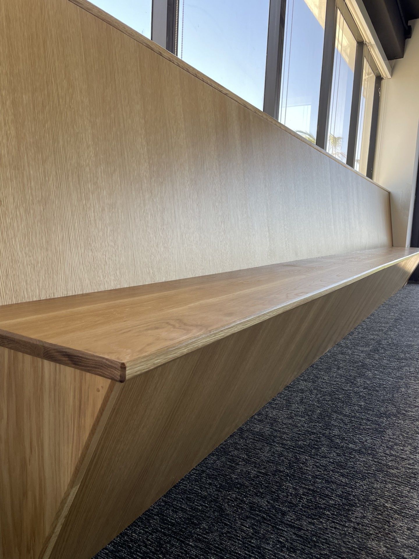 A long wooden bench is sitting next to a window in a room.