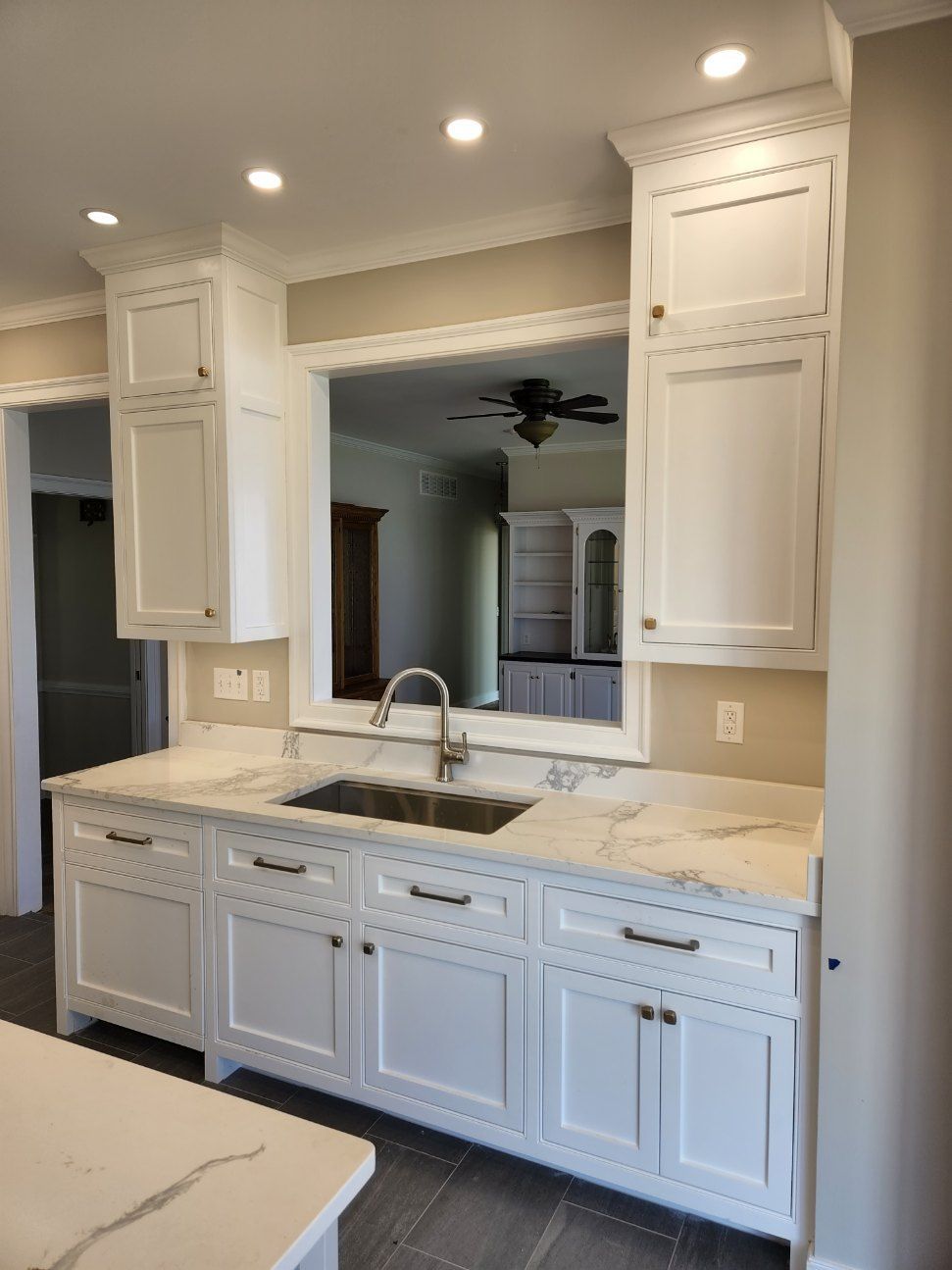 A kitchen with white cabinets, granite counter tops, a sink and a mirror.