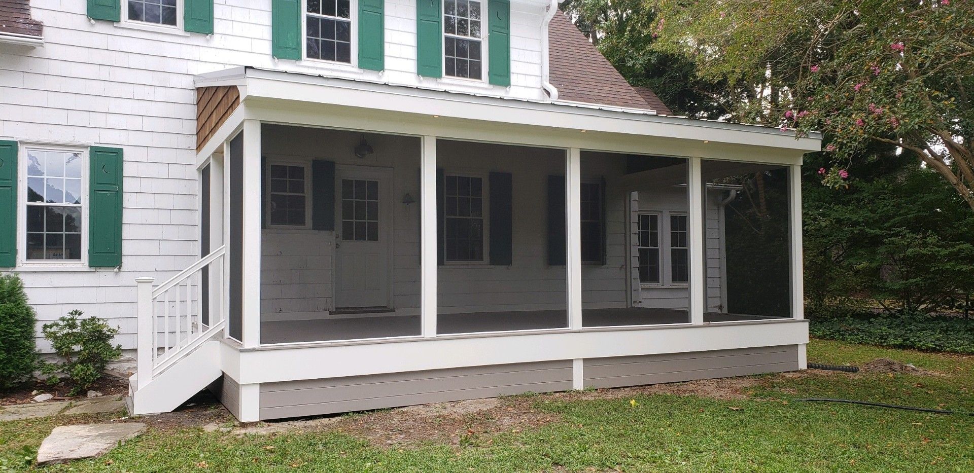 A white house with green shutters and a screened in porch.