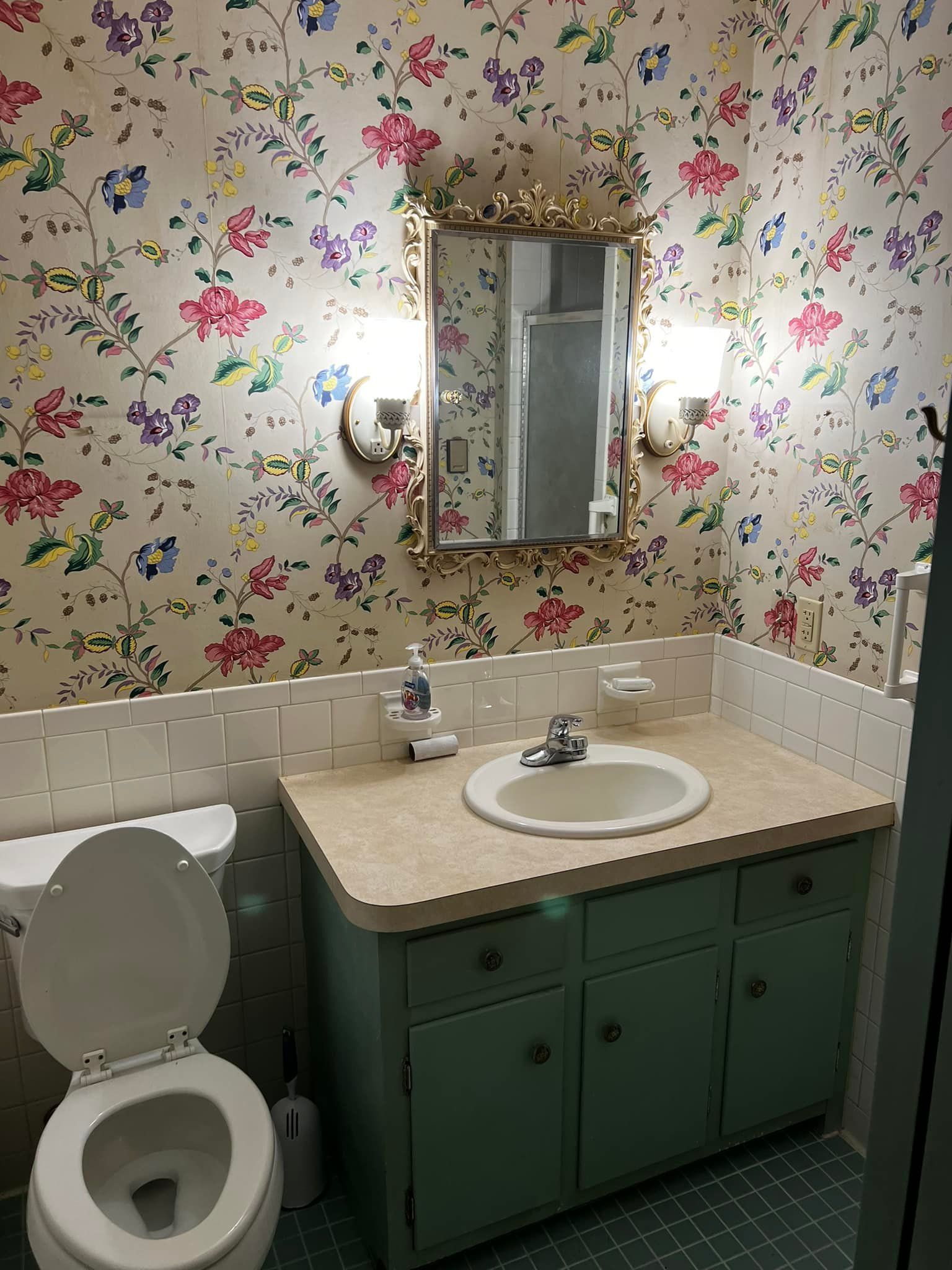 A bathroom with a toilet , sink , mirror and floral wallpaper.
