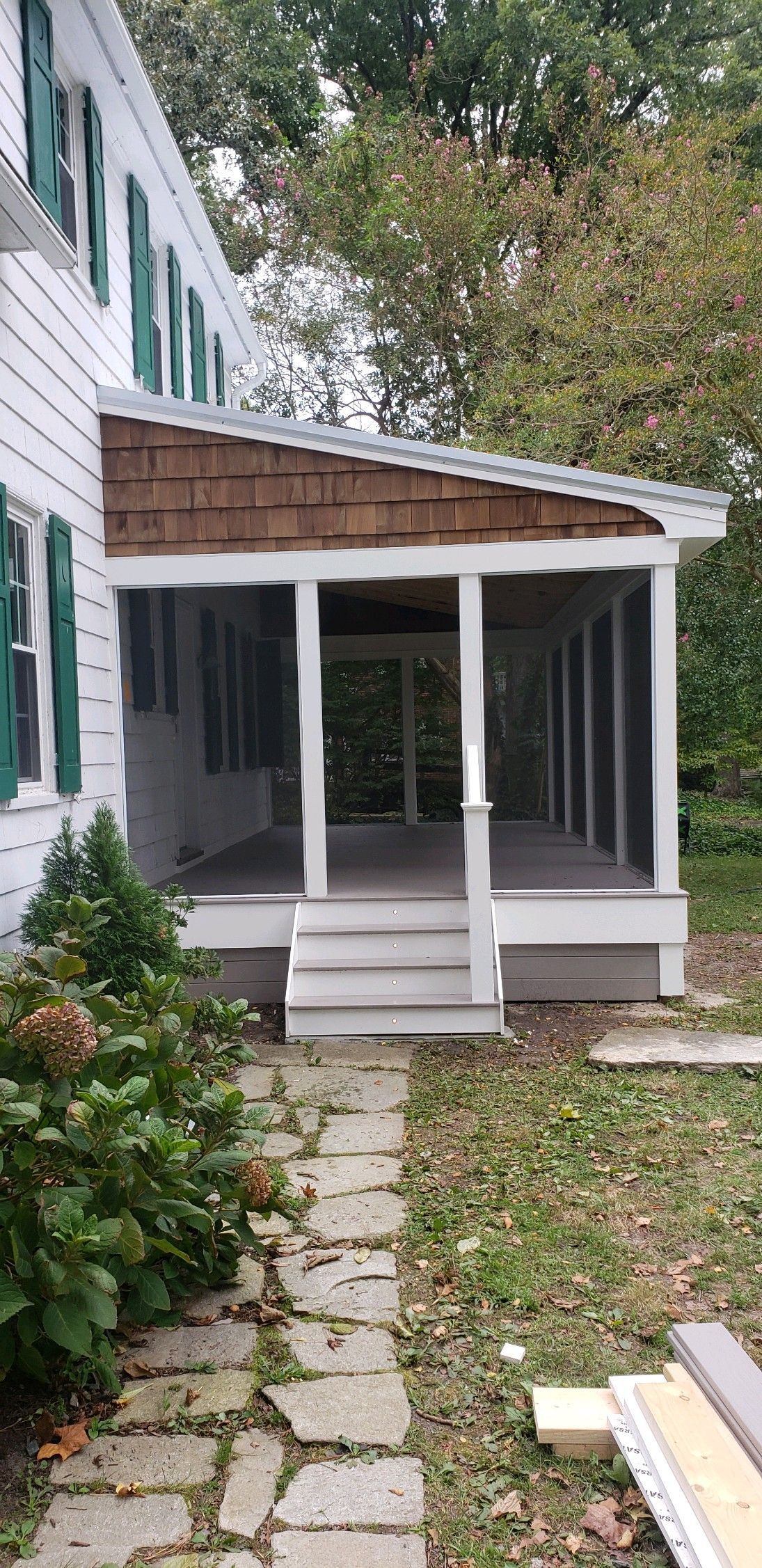 A screened in porch is being built on the side of a white house.