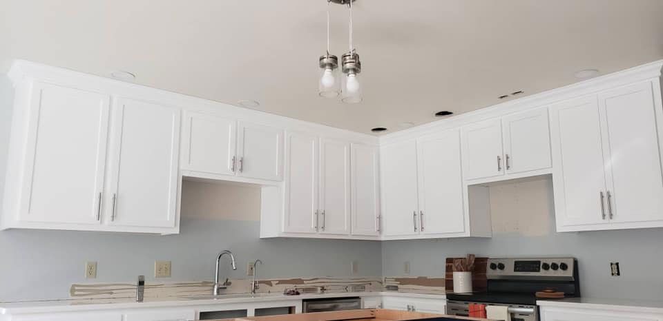 A kitchen with white cabinets , a stove , a sink , and a chandelier hanging from the ceiling.