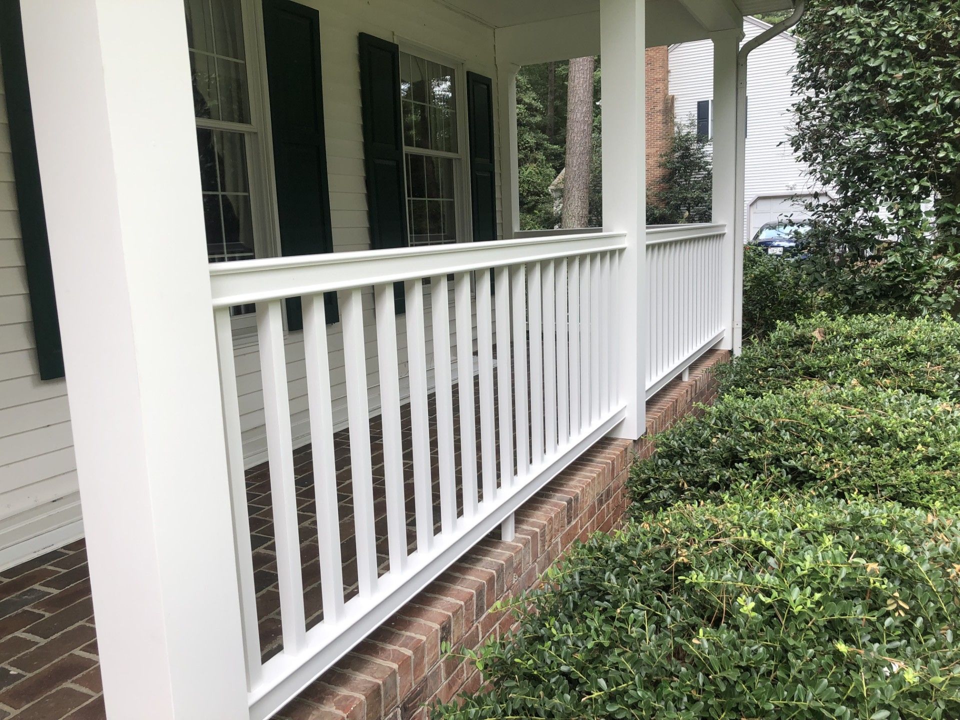 A white railing on a porch of a house with black shutters.