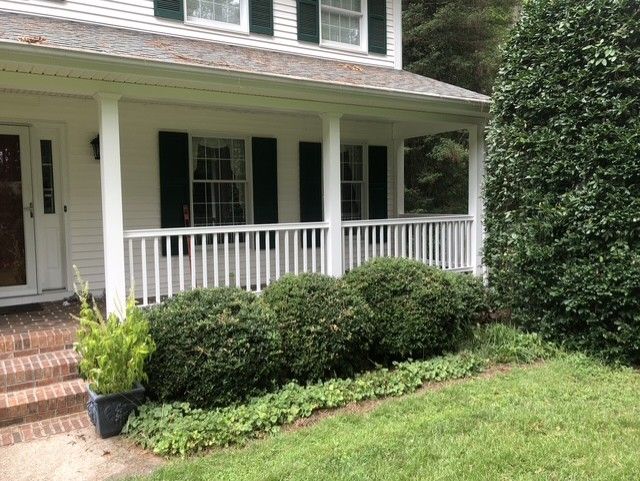 A white house with a porch and black shutters.