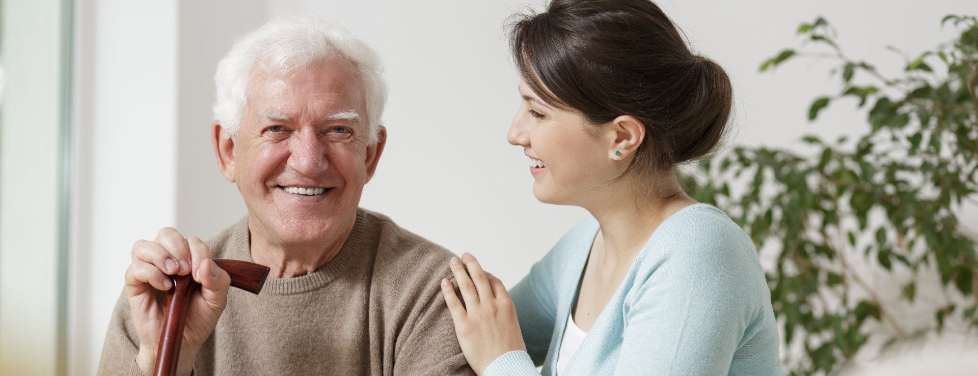 An elderly man with white hair smiles as a woman puts a hand on his shoulder.