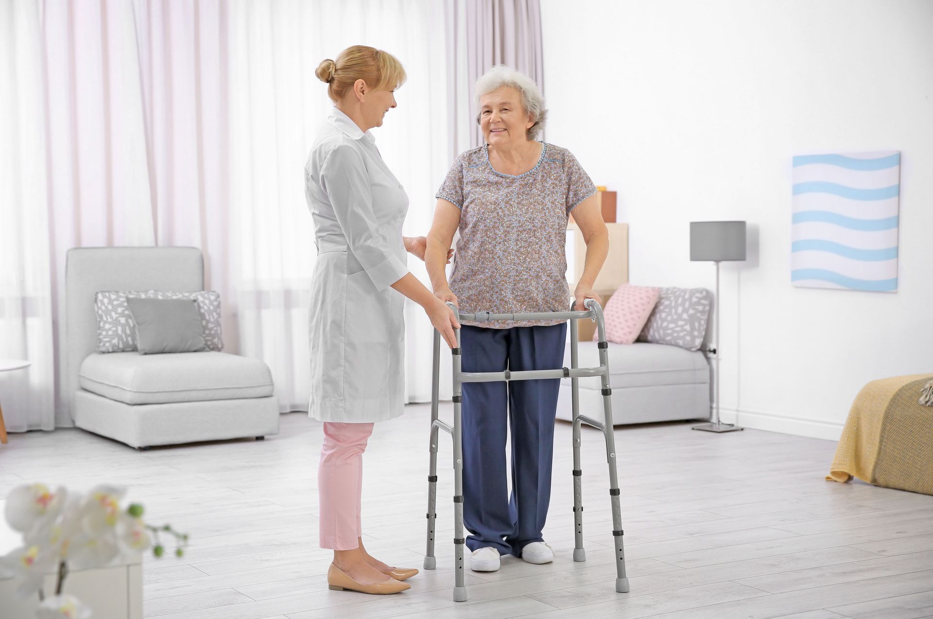 Caregiver assists an elderly woman using a walker in a bright living room.