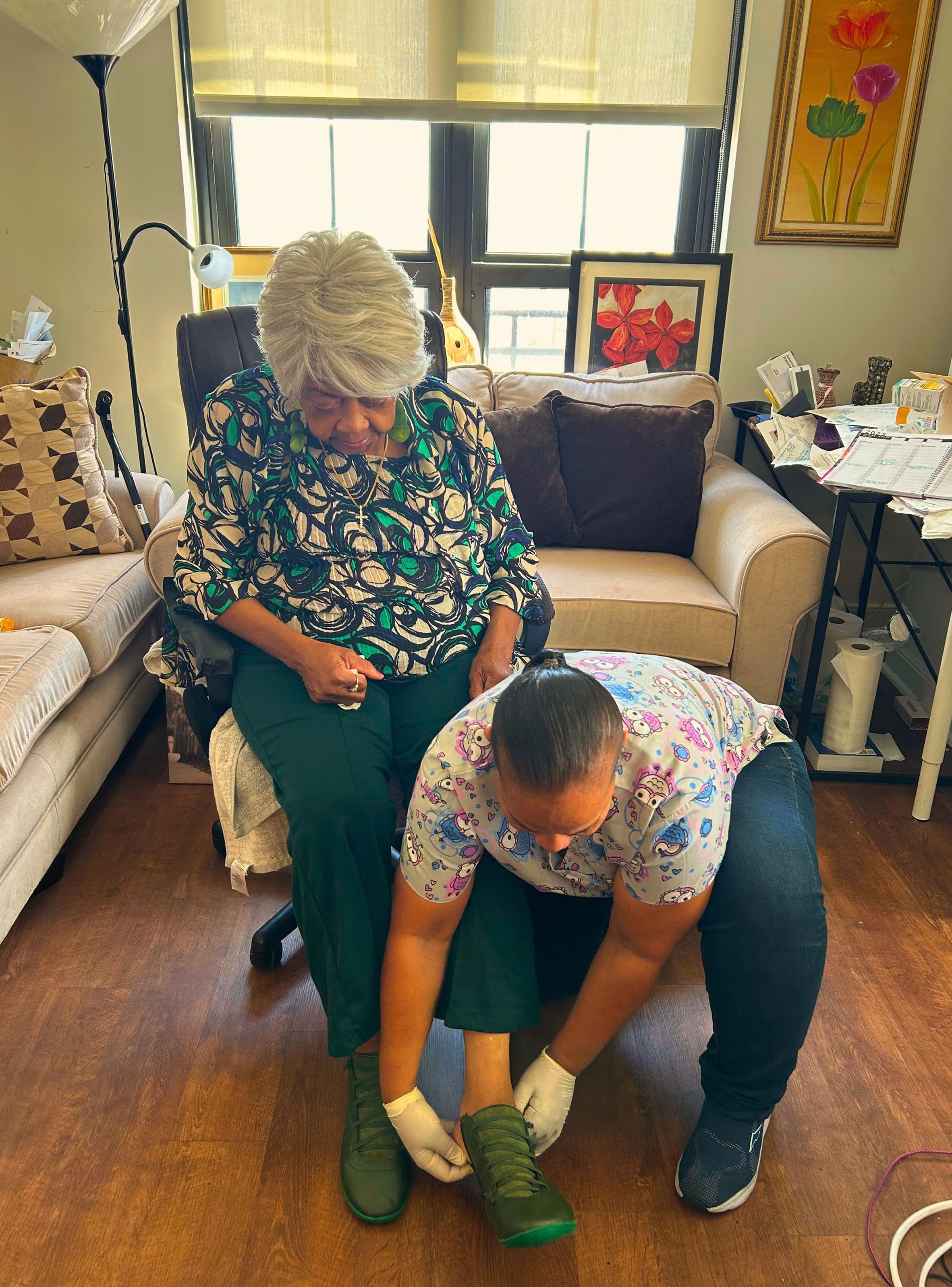 Caregiver tying shoe of an elderly woman in a home setting.