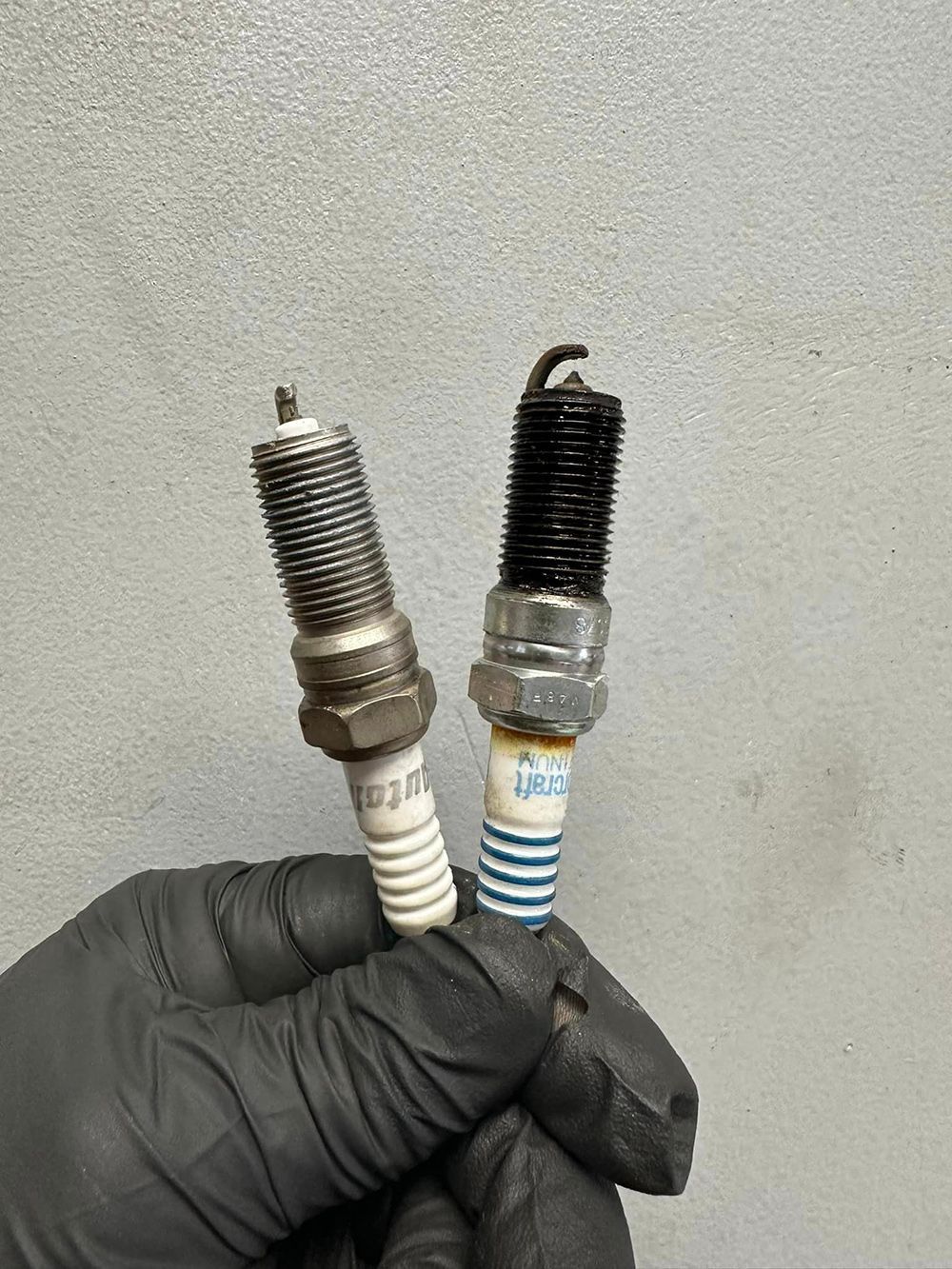 A person is holding two different types of spark plugs in their hand.