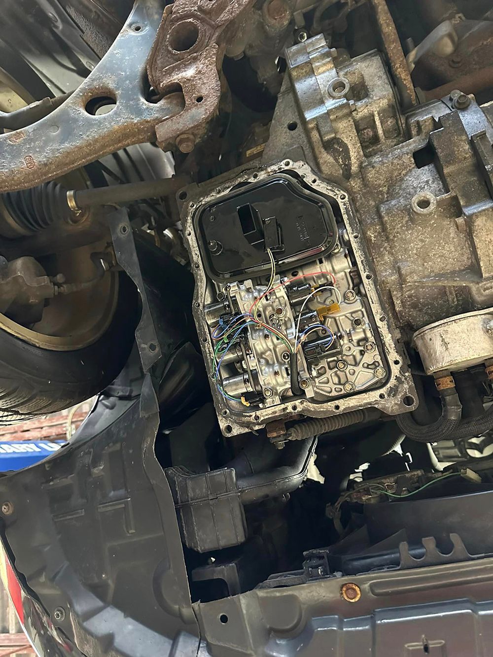 A close up of a dirty transmission on a car.