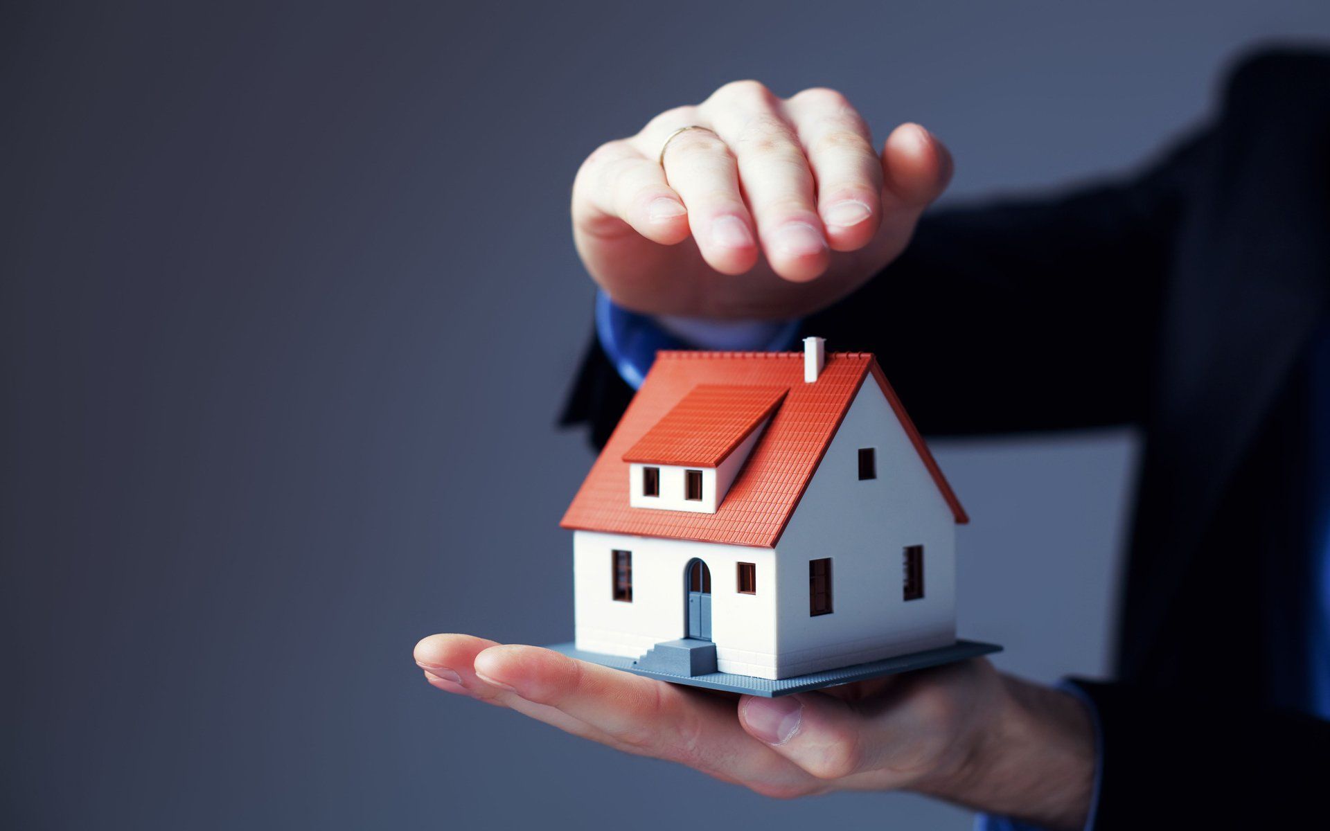 Hand placing a miniature house model on an open palm against a dark background