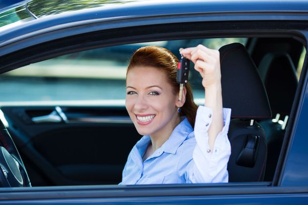 Smiling driver holding car keys out the open window of a blue car