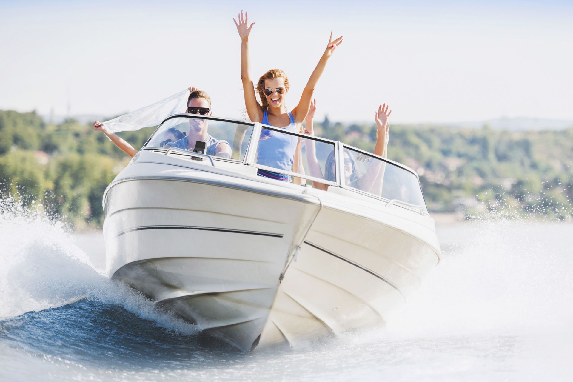 Two people celebrating on a white speedboat, spraying water across a sunny lake