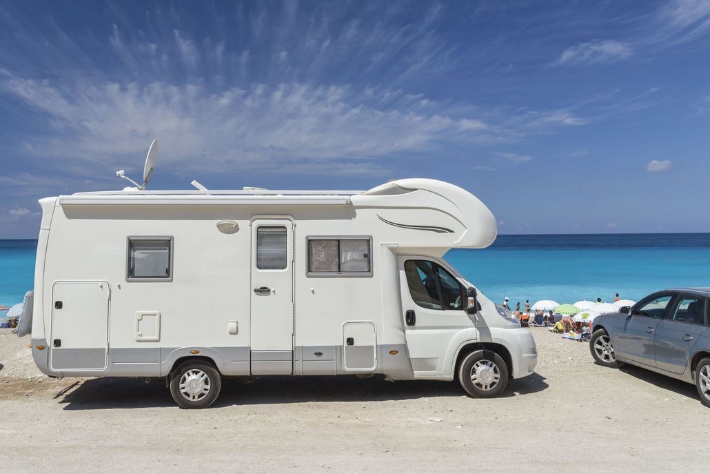 White camper van parked on a sunny beach beside a turquoise sea and another car
