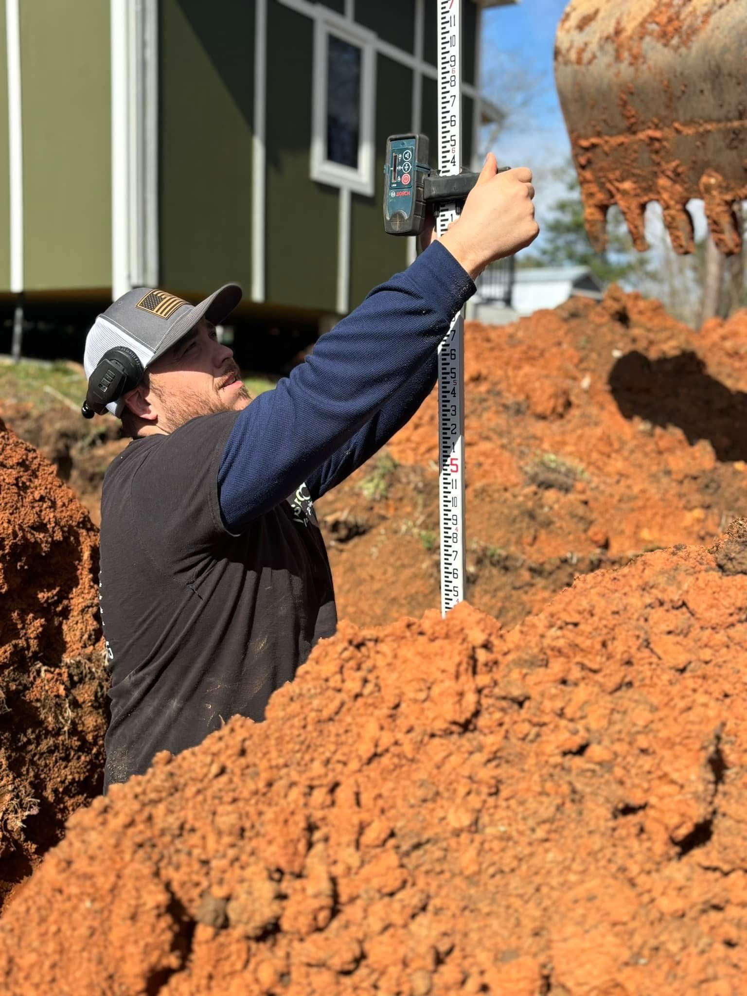 Worker measuring a dirt pile beside a concrete mixer at a construction site