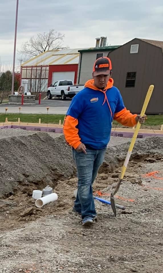 Person in blue and orange work clothes holding a shovel at a construction site.
