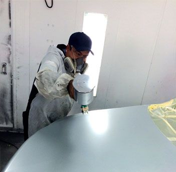 Mechanic spraying gray paint on a car's hood