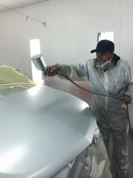 Mechanic spraying gray paint on a car's hood