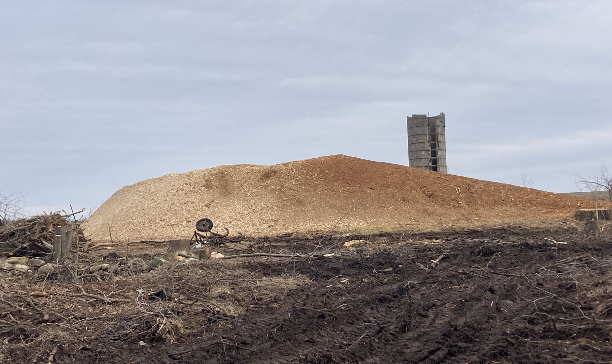 Large pile of tan material with a tall stone structure in the background, set against a cloudy sky.