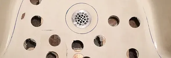 A close up of a sink with holes in it and a drain.