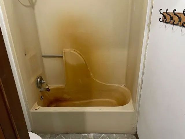 A bathroom with a dirty bathtub and shower stall.