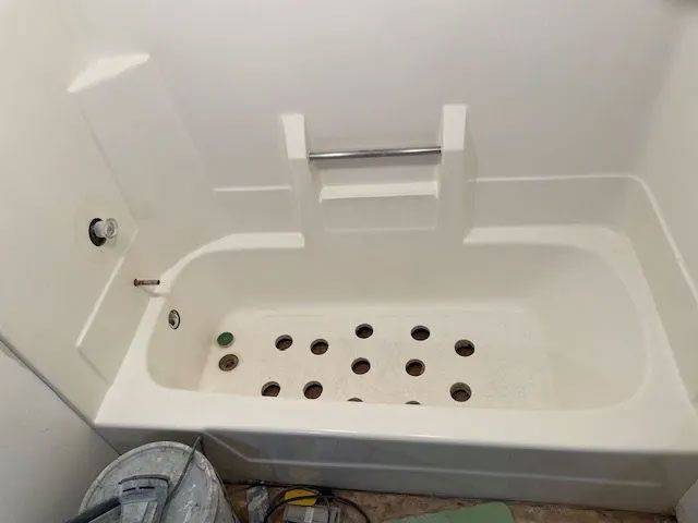A white bathtub with holes in it is in a bathroom.