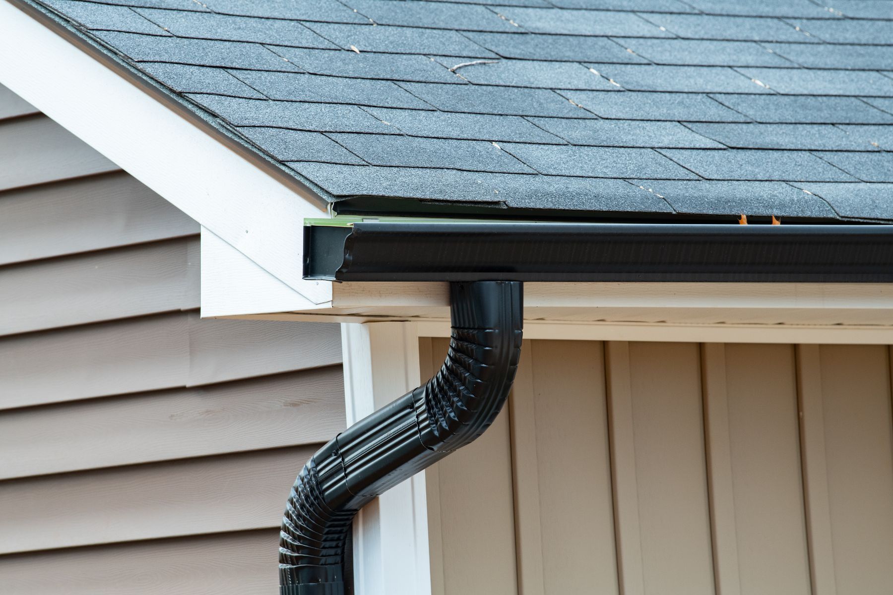 A close up of a black gutter on the side of a house.