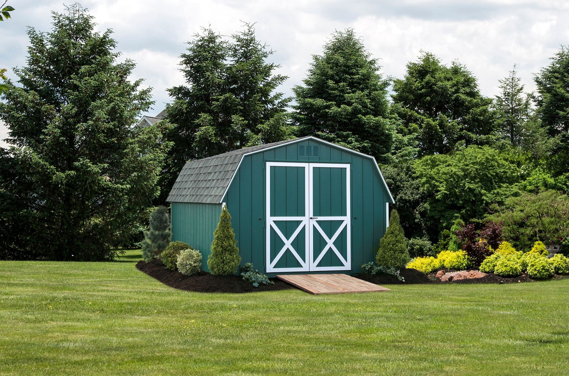 A green barn is sitting in the middle of a lush green field.
