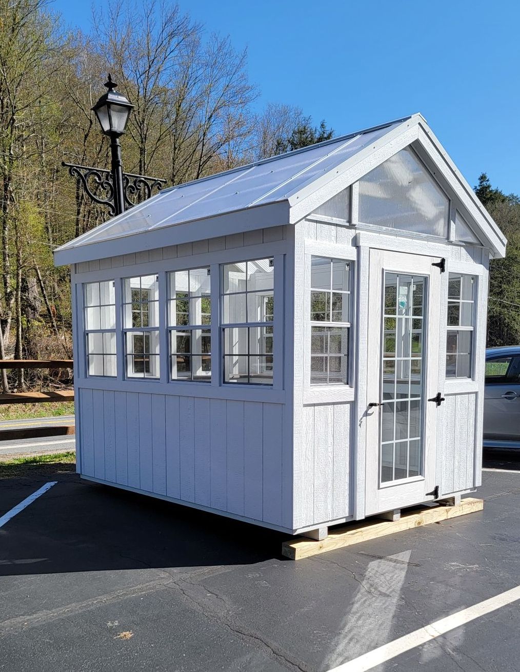A small white shed with lots of windows is in a parking lot.
