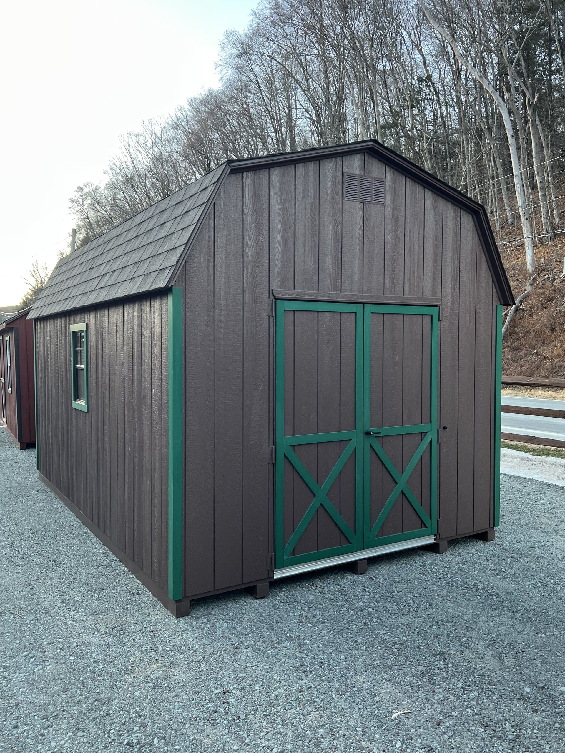 A brown barn with green doors is sitting on top of a gravel lot.