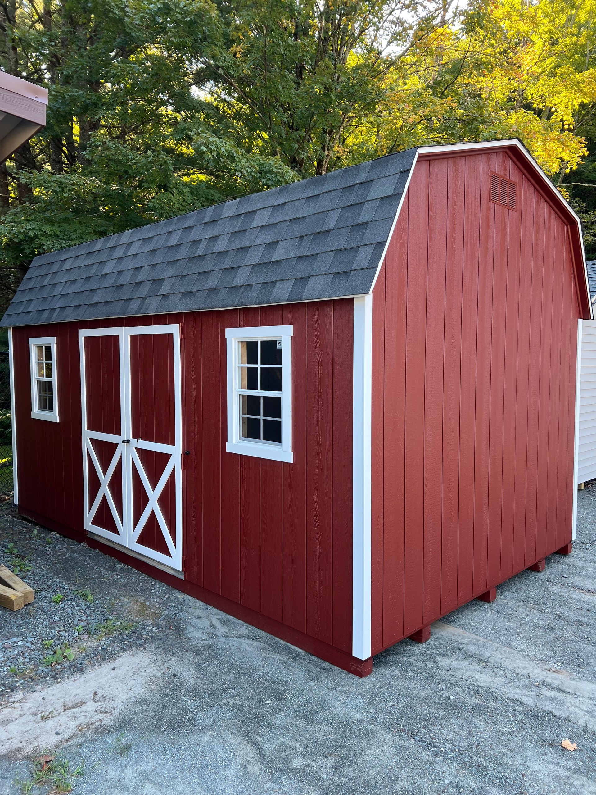 A red barn with a black roof and white trim is sitting on top of a gravel driveway.