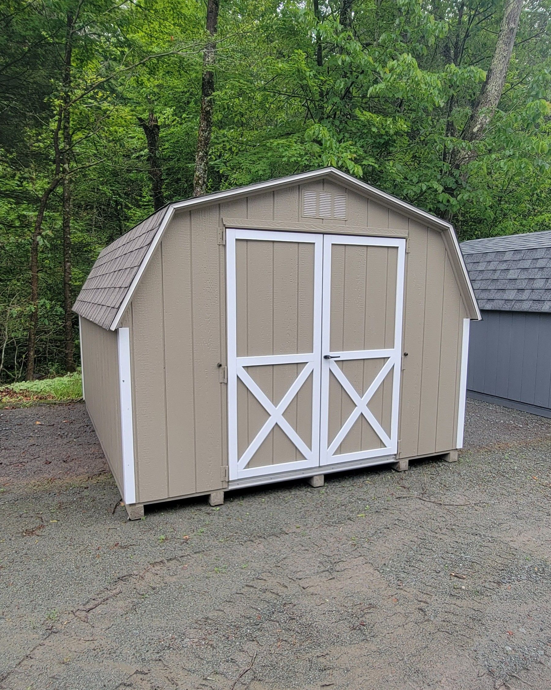 A barn shed with white doors is sitting on top of a gravel lot.
