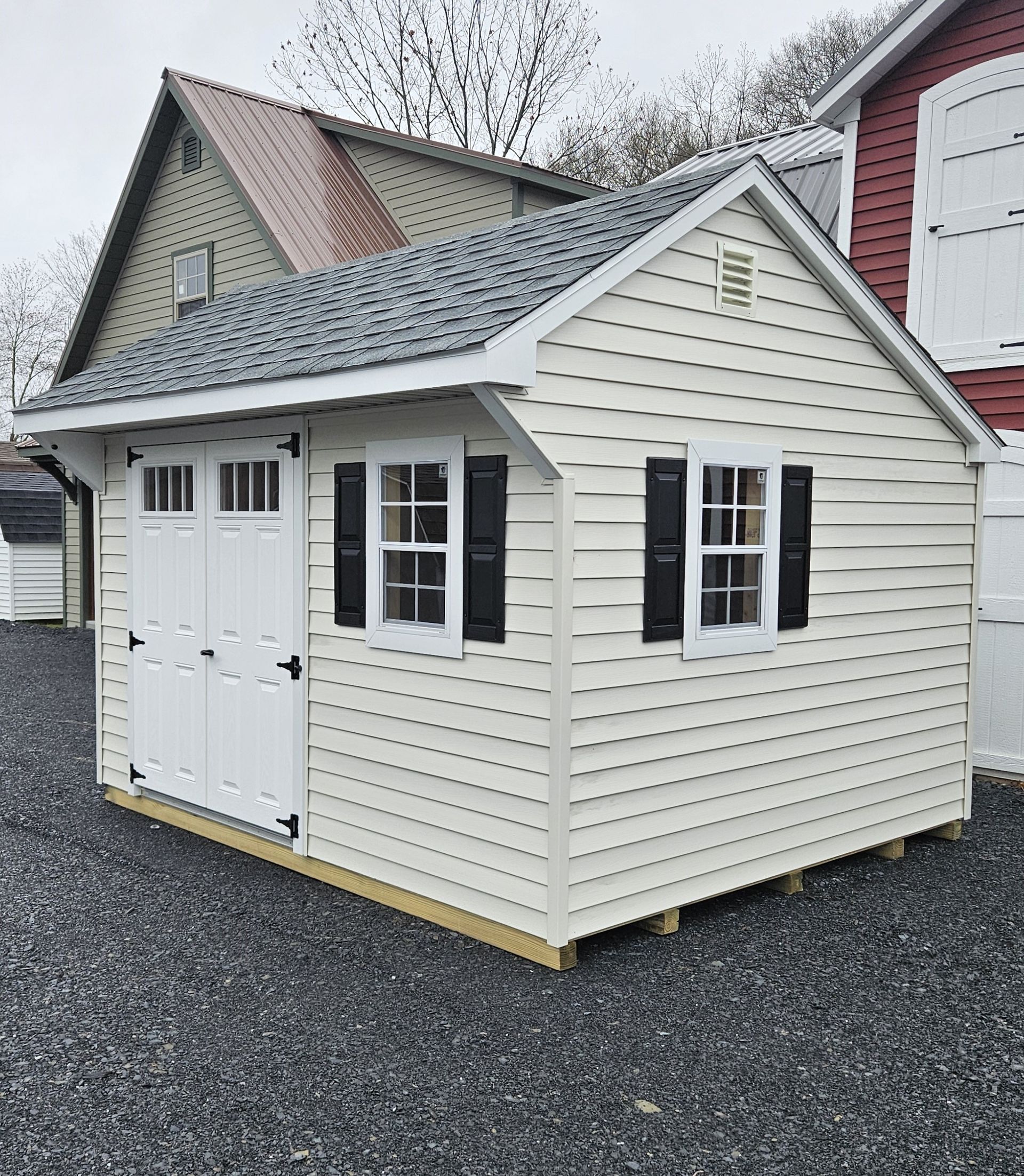A white shed with black shutters is sitting in front of a red house.